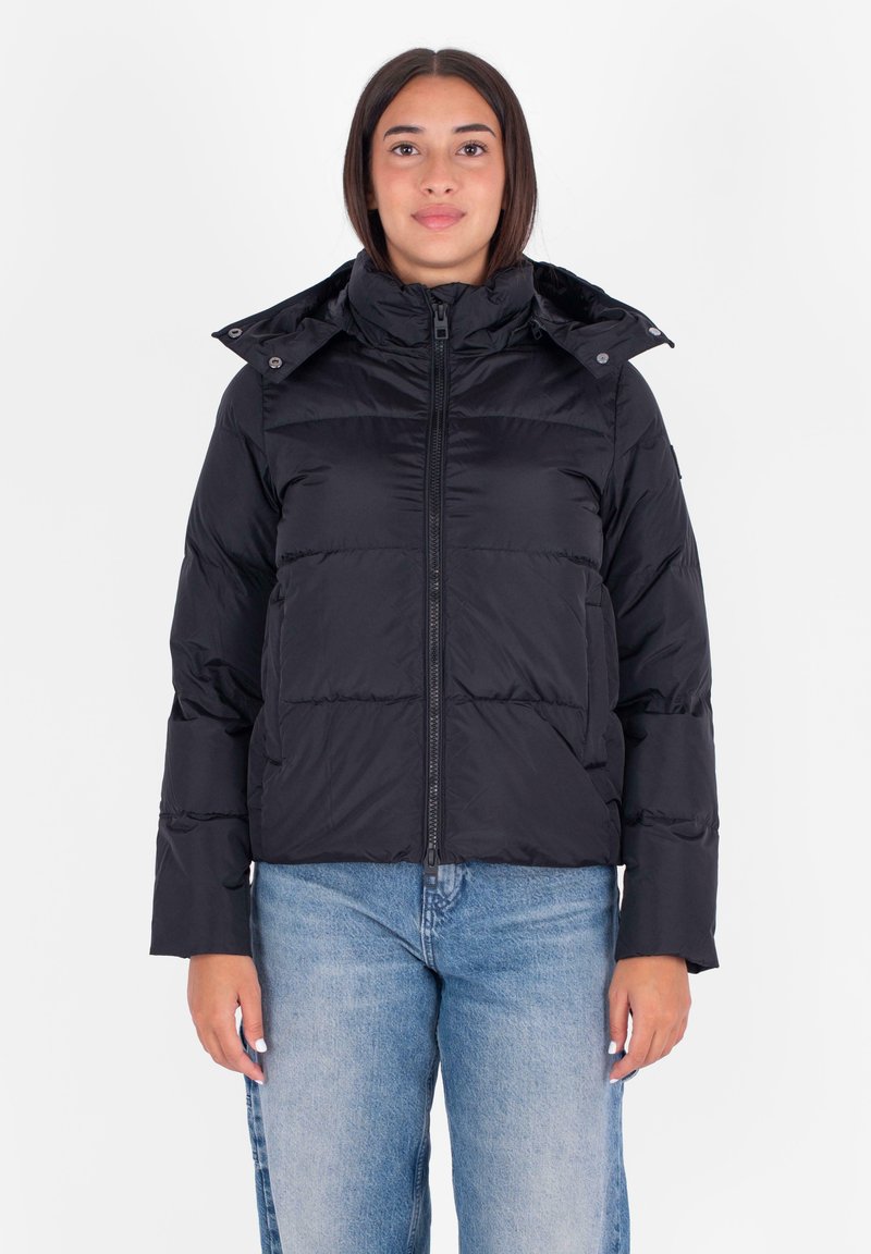 Giacca a vento nera con colletto alto, zip frontale e cappuccio staccabile. Presenta una texture trapuntata e tasche laterali. Abbinata a jeans azzurri chiari.