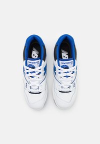 Pair of white New Balance 550 sneakers with blue and black accents, white laces, and visible branding on tongue and side.