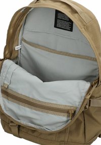 Intérieur du sac à dos beige avec une doublure grise, comportant une poche zippée et un grand compartiment principal. Tissu durable avec des coutures renforcées.