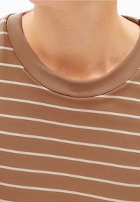 Hnědé pruhované tričko s kulatým výstřihem. Látka působí měkce, s kontrastními bílými pruhy vedoucími vodorovně.