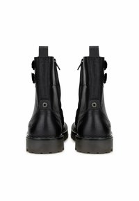 Botas de tobillo de cuero negro con una textura suave, que cuentan con cremalleras laterales dobles y hebillas decorativas, montadas sobre una suela negra gruesa.