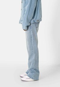 Jeans de mezclilla azul claro con diseño de pierna recta, que presentan un lavado sutil y un estilo tradicional de cinco bolsillos, combinados con zapatillas blancas.