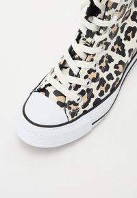 Høye sneakers med en beige og svart leopardmønstret kanvas overdel, hvit gummitoe-kappe, og hvite snørebånd med metalløye.