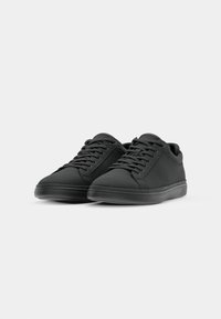 Black sneakers with a smooth, matte finish. Features rounded toe, flat laces, and a low-top design. Textured upper and rubber sole.