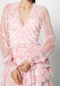 Abito a strati rosa con rouches arruffati, maniche lunghe trasparenti, scollatura a V e tessuto floreale texturizzato. Design texturizzato e leggero.