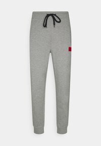 Pantalones jogger grises hechos de tejido suave, con una cintura elástica, cordón negro y una etiqueta de logo roja en el lado izquierdo.