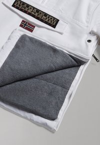Veste isolée blanche avec une doublure en polaire gris doux. Présente une étiquette noire avec "Napapijri" et un petit patch du drapeau norvégien.