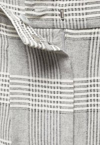 Gros plan sur un tissu à carreaux gris et blanc avec un bouton et une fermeture à clapet en métal sur un rabat replié.