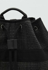 Bolso negro de tejido trenzado con un asa redondeada, que presenta cordones pasados por ojetes de metal y un cuerpo de tela texturizada.