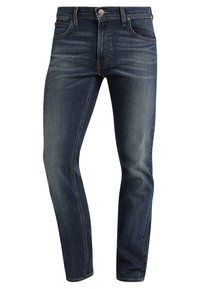 Vaqueros de mezclilla azul oscuro con un corte ajustado, sutiles desgastes en los muslos y diseño estándar de cinco bolsillos. Cuenta con cierre de botón metálico.