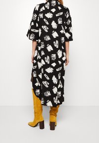 Czarna sukienka z białymi wzorami w formie pociągnięć pędzla, krótki rękaw, asymetryczny dół, w połączeniu z żółtymi zamszowymi kozakami do kolan na grubym obcasie.