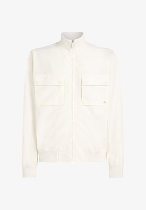 Világos krémszínű bomber dzseki sima anyagból, magas gallérral, elöl cipzárral és két mellkaszsebbel, amelyek fedeles záródásúak. Bordázott mandzsetták.