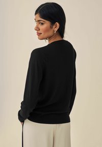 Pull noir en tricot avec un col rond et des manches longues. Texture lisse avec une taille ajustée, vu de côté.