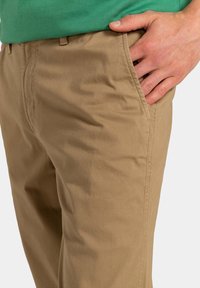 Beige bomulds-chinos med subtil tekstur, med lige pasform og sidelommer. Livvidden har en bæltestrop og minimalistisk syning.