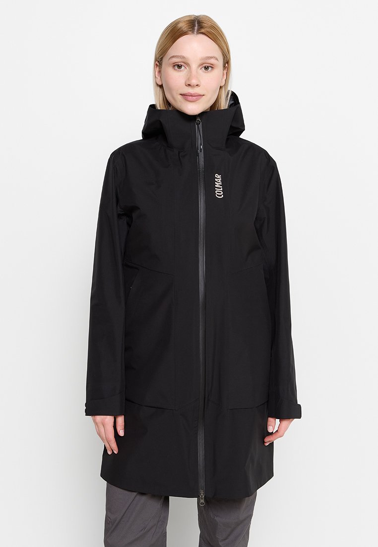 Cappotto lungo nero impermeabile con colletto alto e zip frontale, dotato di due tasche anteriori e di un logo discreto sul lato sinistro.