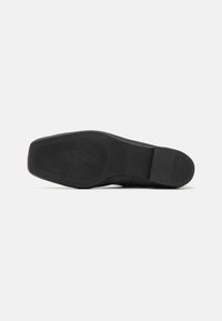 Semelle de chaussure noire avec une surface lisse, présentant un motif texturé pour l'adhérence et un léger talon. Aucune marque ou accent visible.