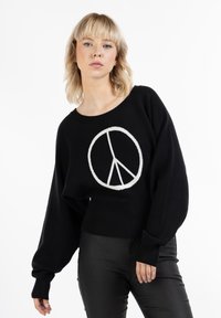Maglione a maglia nera con un grafico del simbolo della pace bianco, con maniche lunghe e un design corto. Abbinato a pantaloni neri.