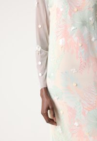 Transparante jurk met pastel bloemenontwerp in roze, groen en crèmekleuren. Versierd met ronde pailletten en textuurelementen.