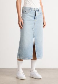 Lys blå denimskjørt med en frontsplitt, midt på leggen, og casual passform, kombinert med hvite sneakers og ribbede hvite sokker.