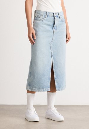 Light blue denim skirt with a front slit, mid-calf length, and casual fit, paired with white sneakers and ribbed white socks.