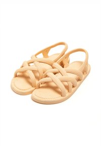 Beige sandals made of textured rubber, featuring crisscross straps and an open back for easy wear. Flat sole with a patterned footbed.