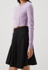 Crop top lilla a coste con maniche lunghe e dettaglio della cucitura frontale abbinato a una gonna nera plissettata, caratterizzata da una superficie liscia e una forma svasata.