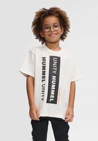Lysfarvet bomulds t-shirt med fed sort og orange tekst. Korte ærmer, afslappet pasform og rund halsudskæring.
