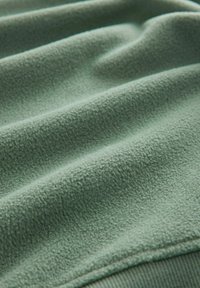 Grøn fleece stof med en blød, struktureret overflade, der viser bølger og folder, der fremhæver dets tykkelse og blødhed.