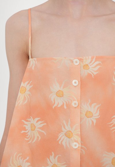 Perzikkleurig tanktop met bloemenpatroon, voorzien van kleine knopen aan de voorkant en dunne schouderbandjes. Gemaakt van een lichtgewicht stof met een zachte textuur.