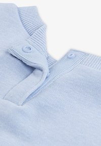 Light blue polo shirt featuring a ribbed collar, two button placket, and soft textured fabric. Seam detail visible at neckline.