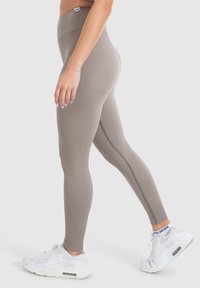 Geribbelde, high-waisted legging in licht taupe met een gladde textuur en details in de zijnaad. Gecombineerd met witte sport sneakers.