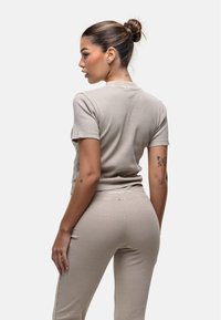 Completo in tessuto a coste in un beige chiaro, composto da una maglietta attillata a maniche corte e pantaloni a vita alta, con un logo discreto sulla cintura.