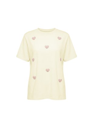 Kortærmet cremefarvet T-shirt dekoreret med jævnt fordelte små lyserøde broderede hjertepatches på forsiden.