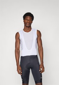 Maillot de cyclisme sans manches en mesh blanc avec un col rond et un design découpé, associé à un cuissard rembourré noir avec poches latérales.