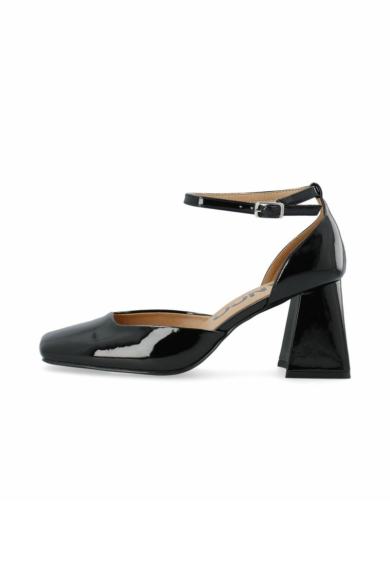 Pump en cuir verni noir avec un bout carré et un talon bloc épais. Présente une sangle à la cheville avec une boucle en argent et une doublure intérieure lisse.