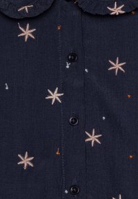 Tessuto blu navy con stelle bianche ricamate e piccoli punti arancioni e azzurri, con bottoni neri lungo il centro.