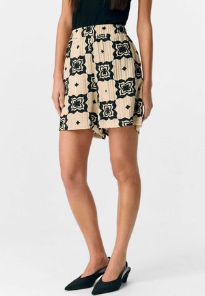 Shorts noirs et crème à motif avec un design plissé, taille haute et fentes sur les côtés. Le tissu a une apparence texturée.