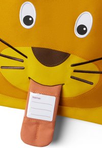 Yellow fabric storage bag with a lion face design, featuring large eyes, whiskers, and a tongue-shaped tag for names.