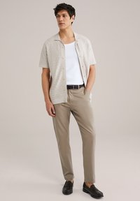 Camicia a maniche corte texture beige chiaro con bottoni chiari, canottiera bianca, pantaloni khaki chiaro e mocassini neri. Design semplice, vestibilità casual.