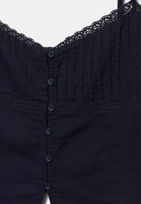Blouse sans manches bleu marine avec des plis verticaux, un bord en dentelle le long de l'encolure et du milieu, et une rangée frontale de six petits boutons.
