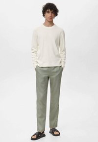 Pull blanc à côtes, pantalon taillé vert clair, sandales noires à enfiler. Design minimaliste avec une coupe décontractée.