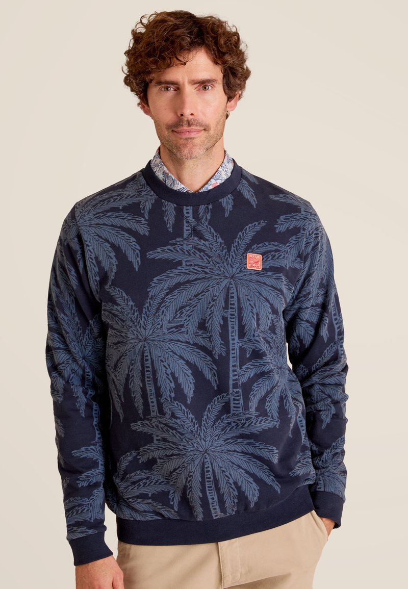 Sweatshirt marine avec un motif de palmier en bleu clair. Encolure ras du cou et poignets côtelés. Petit patch logo rouge près de la poitrine.