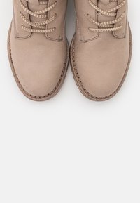 Botas beige con cordones, acabado texturizado, punta redonda, suela marrón en contraste y cordones tejidos texturizados. Diseño limpio y minimalista.