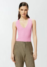 Top senza maniche a coste rosa con scollatura a V profonda, abbinato a pantaloni marroni a vita alta con texture e chiusura con bottone.