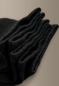 Pile de chaussettes en maille côtelée noire disposées sur une surface beige, montrant la texture et les couches pliées.