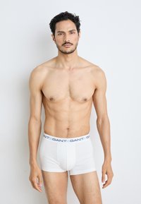Boxer-briefs en coton blanc avec une ceinture de marque bleu et blanc, présentant un design ajusté et une texture lisse.