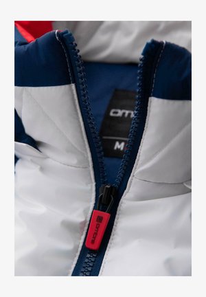 Giacca imbottita con un esterno bianco e dettagli blu navy. Presenta una chiusura con zip frontale dotata di un tirante rosso e un'etichetta con il nome del marchio.
