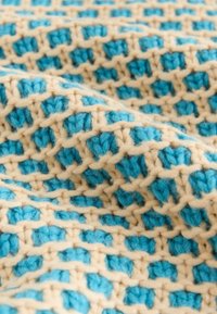 Crochet-heittotyyny, jossa on pehmeä rakenne, vuorottelevat turkoosi ja kermankeltaiset neliöt, irtonainen kudonta ja näkyvät langan kuidut.