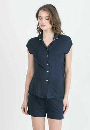Tummansininen lyhythihainen pyjama-setti, jossa on napitettavissa oleva paita, jossa on valkoiset reunukset, sekä yhdistelevät shortsit, valmistettu pehmeästä ja kevyestä kankaasta.