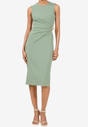 Miętowozielona sukienka bez rękawów, do kolan, z marszczeniem po boku i złotą sprzączką, noszona z beżowymi szpilkami z paskiem wokół kostki.